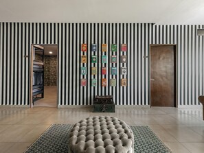 Ein Zimmer mit einer gestreiften Wand, einem runden Ottomanen und einem Koffer auf einem Teppich.