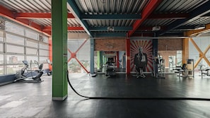 Ein Fitnessraum mit Trainingsgeräten, großen Fenstern und einer Ziegelwand.