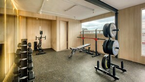 Academia com equipamentos de musculação, um banco e um espelho.