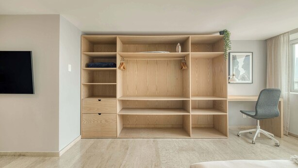 Een kamer met een ingebouwde houten garderobe, een bureau met stoel, een flatscreen televisie aan de muur en een lijst met een afbeelding.