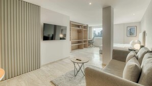 Een moderne hotelkamer met een flatscreen televisie, een bank, een klein rond tafeltje, een kast en uitzicht op de stad.