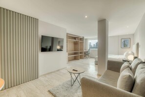 A modern hotel room with a flat-screen TV, a sofa, a small round table, a closet, and a city view. - Modern King Studio in Central Roma Norte (Ciudad de México)