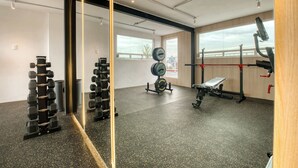 Een sportschool met gewichthefapparatuur, een bank en een grote spiegel.