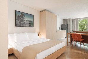 A hotel room with a bed, a desk, a chair, a refrigerator, and a window with a view. - Modern Loft with Balcony & View of Parque Mexico (Ciudad de México)