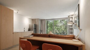 A modern kitchen with a wooden countertop, two orange chairs, a wooden dining table, and a view of trees through the window. - Modern Loft with Balcony & View of Parque Mexico (Ciudad de México)