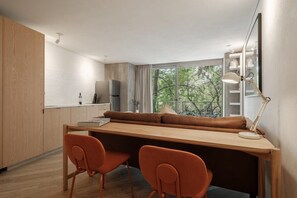 A modern kitchen with a wooden countertop, two orange chairs, a wooden dining table, and a view of trees through the window. - Modern Loft with Balcony & View of Parque Mexico (Ciudad de México)