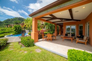 Ein überdachter Außenbereich mit Pool, Sitzgelegenheiten und Blick auf eine üppige Landschaft.