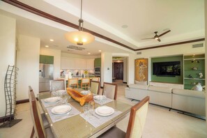 Un coin repas avec une table dressée pour quatre personnes, un ventilateur de plafond et une cuisine en arrière-plan.