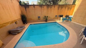 Ein rechteckiger Swimmingpool mit Fliesenrand, eine Liege, ein kleiner Luftmatratze und ein Blumentopf.