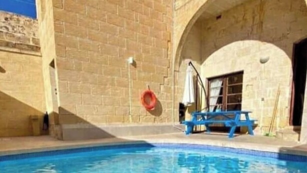 Une piscine à l’eau d’un bleu cristallin, entourée de murs en pierre et agrémentée d’un fauteuil de jardin bleu.