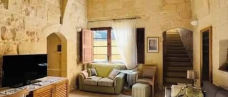 Una habitación de paredes de piedra con una televisión, sofás, una mesa de centro y una escalera.