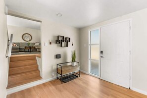 A hallway with a wooden floor, a white door, a staircase, a wall-mounted shelf with a plant, and a wall clock. - Family Friendly Retreat with Game Room Huge Yard (Arvada)