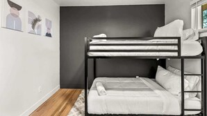 Quarto com beliche, parede escura, roupa de cama branca e tapete felpudo.