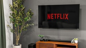 Uma sala de estar moderna com uma televisão de tela plana grande fixada em uma parede cinza, um móvel de entretenimento de madeira abaixo e um vaso de planta à esquerda.