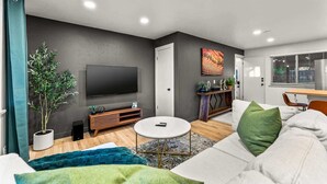 Uma sala de estar moderna com televisão de tela plana, um sofá, uma mesa de centro e um espaço de jantar com mesa e cadeiras.
