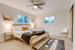 A bedroom with a bed, bedside tables, a ceiling fan, windows, and a chair. - Hot Tub Modern Home Great Location (Arvada)