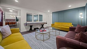 Uma sala de estar moderna com um sofá amarelo, um sofá rosa, uma mesa de centro e uma área de jantar ao fundo.