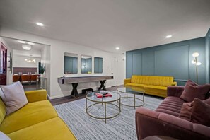 Ein modernes Wohnzimmer mit einem gelben Sofa, einem pinken Sofa, einem Couchtisch und einem Essbereich im Hintergrund.