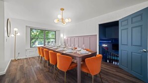 Uma sala de jantar com uma mesa comprida posta para seis pessoas, soalho de madeira e uma porta azul.