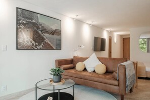 A modern living room with a brown leather sofa, a glass coffee table, and a large framed picture on the wall. - Modern Loft with Balcony & View of Parque Mexico (Ciudad de México)