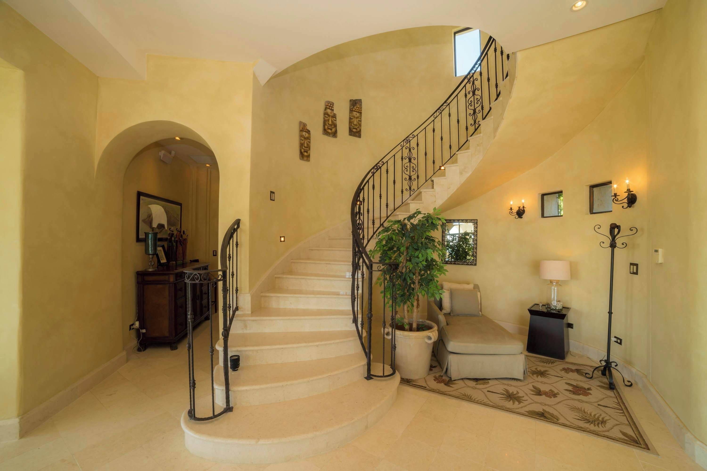 A grand staircase with a curved design, a potted plant, a seating area, and wall-mounted lighting.