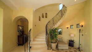 A grand staircase with a curved design, a potted plant, a seating area, and wall-mounted lighting. - Casa Puesta del Sol 5 bdr - Ocean View Family (Playa Herradura)