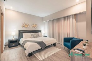 A modern hotel room with a large bed, a blue armchair, a small table with a remote control, and a decorative wall piece. - Regatta Living Ii with Breakfast Included! - 705 (Santo Domingo)