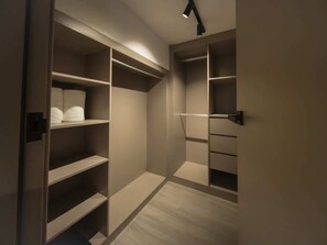 Ein begehbarer Kleiderschrank mit mehreren Regalen und Schubladen, einer Lampe und Holzboden.