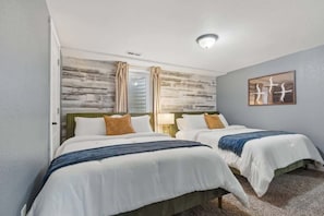 A hotel room with two beds, a wooden accent wall, a ceiling light, and a framed artwork. - Projector Nights & Park Delights I Designer Reno (Arvada)
