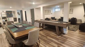 Una sala moderna con mesa de billar, comedor con una mesa larga y sillas, y un conjunto de sofás.