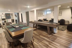 A modern living room with a pool table, a dining area with a long table and chairs, and a sofa set.