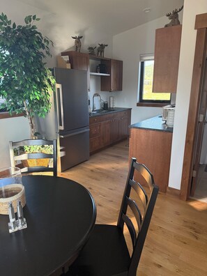 A compact kitchen with wooden cabinets, a built-in refrigerator, a dining table with chairs, and a potted plant. - Serene 1-bedroom + 3-bunk bed Bungalow in Big Sky near Town Center (Big Sky)