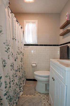 A bathroom with a toilet, a shower curtain with a floral pattern, a toilet paper holder, and a towel rack. - The Bulldog Farmhouse - 100+ year old home (Athens)