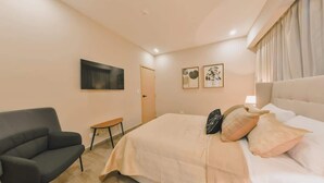 Ein Schlafzimmer mit Bett, einem Sessel, einem kleinen Tisch und Bildern an den Wänden.