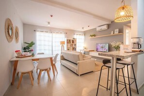 Een moderne woonkamer met een bank, eettafel, stoelen en een keukenhoek met een koffieapparaat.