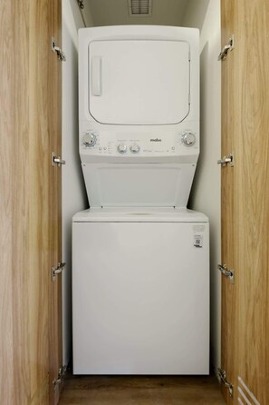 Eine kompakte, weiße Waschmaschine und Trockner-Kombination in einem Holzschrank mit Metallverschlüssen.