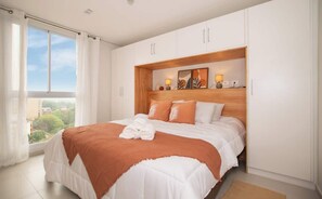 A bedroom with a large bed, white walls, a wooden headboard, and a view through a window. - Sophisticated 1BR Apt, City Views & Great Location (Asunción)