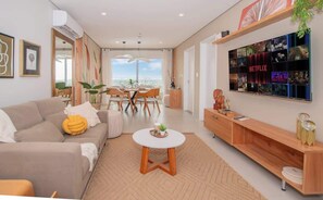 A modern living room with a sofa, coffee table, TV, and dining area. - Sophisticated 1BR Apt, City Views & Great Location (Asunción)