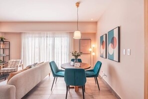A modern living room with a round dining table, teal chairs, a sofa, and a large window with sheer curtains. - Santo Domingo Gem Modern Apartment with Amenities! (Santo Domingo)