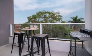 A balcony with two black stools, a small round table with a tray, and a grill station. - Cozy One-Bedroom with Gym & Pool (Asunción)