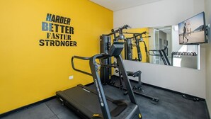 Un gimnasio con cinta de correr, máquinas de pesas y una frase motivacional en la pared.