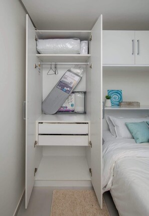 Ein Schlafzimmer mit einem Bett, einem weißen Kleiderschrank mit geöffneten Türen und einer kleinen Pflanze auf dem Nachttisch.