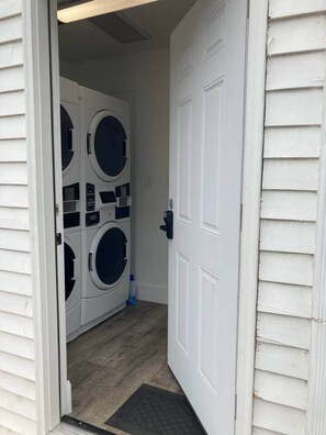 A laundry room with two stacked front-loading washing machines, a door, and a wooden floor. - Downtown Olde Town Arvada- Across from light rail (Arvada)