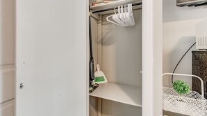 Ein weißer Kleiderschrank mit Regalen, einer Kleiderstange und einer kleinen Pflanze.