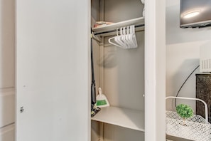 Ein weißer Kleiderschrank mit Regalen, einer Kleiderstange und einer kleinen Pflanze.