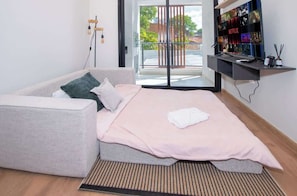 A modern bedroom with a sofa bed, a flat-screen TV, and a view of the outdoors. - Stylish 1BR King bed Pool, Gym, BBQ Prime Area (Asunción)