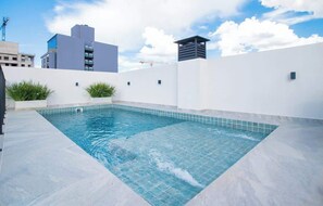 A rooftop swimming pool with a tiled edge, surrounded by white walls and some greenery. - Stylish 1BR King bed Pool, Gym, BBQ Prime Area (Asunción)