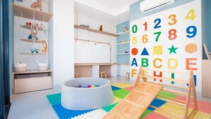 Una sala de juegos infantil con una piscina de pelotas, estanterías de madera y un gran mural del alfabeto.