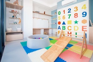 A children's playroom with a ball pit, wooden shelves, and a large alphabet wall.