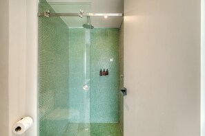 Eine Dusche mit Glastür und grünen Mosaikfliesen.